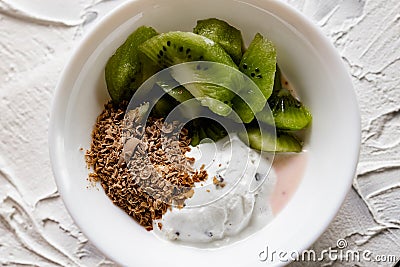 A pair of small dessert bowls with fresh kiwi fruit, white ice cream, yogurt and chocolate chips on a white stone background Stock Photo