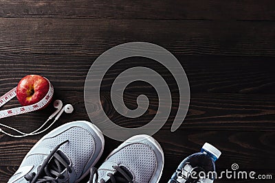 Pair sports shoes, headphones, apple and water bottle on black wood Stock Photo