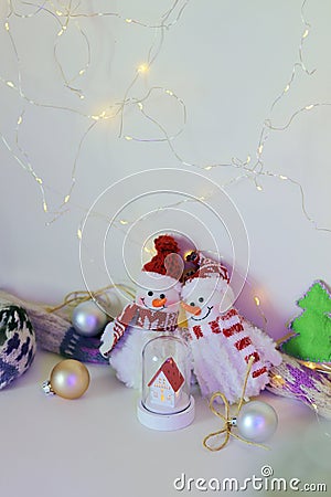 A pair of toy cheerful snowmen with a Christmas tree toy, decor on a light background with illumination Stock Photo