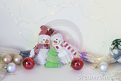 A pair of toy cheerful snowmen with a Christmas tree toy, decor on a light background with illumination Stock Photo