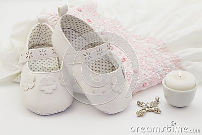 Pair of white baby shoes on embroidered christening white dress, cross and candle Stock Photo