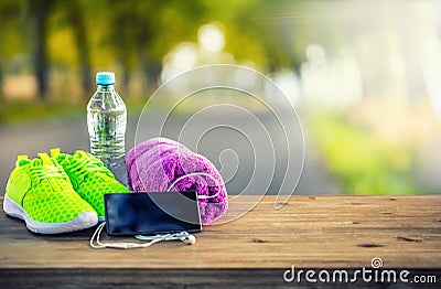 Pair of yellow green sport shoes towel water smart pone and headphones on wooden board. In the background forest or park trail. Stock Photo