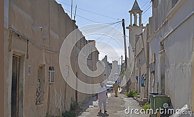 Pakistani man walking on an unpaved street and mosque in an old district of Doha, Qatar Editorial Stock Photo