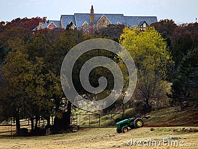 Palatial house almost hidden in trees on hill with country pasture and fence and tractor in foreground Stock Photo
