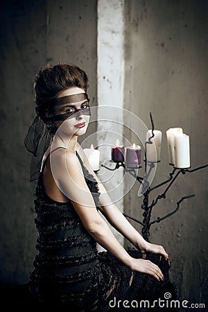 Pale girl with retro style hair in long witch dress with lace face mask in mystical castle Stock Photo