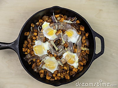 Sweet Potato Hash with Baked Eggs Paleo Diet Meal in Black Cast Iron Pan on Plain Maple Wood Table Stock Photo