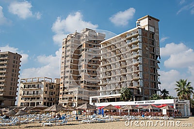 Palm Beach with beach umbrellas and tourists and abandoned hotels atghost town, Famagusta, Northern Cyprus Editorial Stock Photo