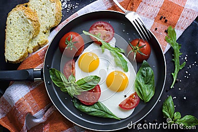 Pan of fried eggs, basil and tomatoes with bread on grunge metallic table surface. Stock Photo