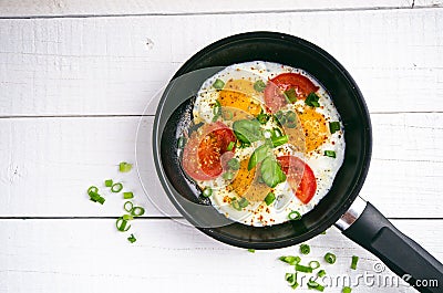 Pan of fried eggs with tomatoes, cheese, spring onion, herbs on a white table. White wooden table. Concept of food. Breakfast time Stock Photo