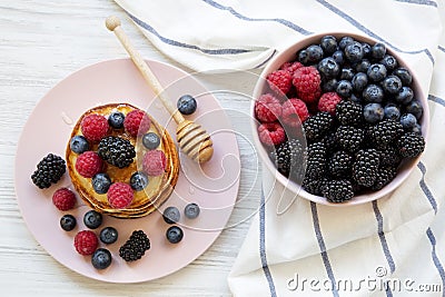 Pancakes with berries and honey on a pink plate, bowl of berries, top view. Stock Photo