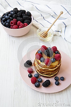 Pancakes with berries and honey on a pink plate over white wooden surface Stock Photo