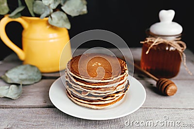 Pancakes with honey on plate, wooden table, spoon, yellow vase with eucalyptus Stock Photo