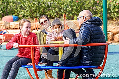 Happy family riding a carousel, spinning in a metal roundabout equipment at a playground on a sunny autumn day. Stock Photo