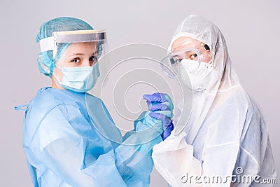 Pandemic. Tired doctors in covid-19 protective gear hold hands in support of a dire situation. Gray background. Stock Photo