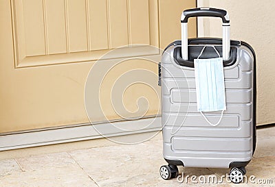 Pandemic travel seen in tan door, gray suitcase, and face mask Stock Photo