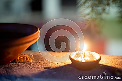 Panning shot of diya oil lamp casting light on a earthenware bird water feeder placed near plants on the hindu festival Stock Photo