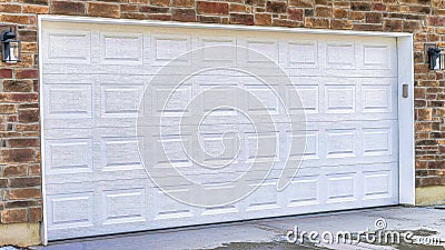 Pano White wooden garage door and wet driveway of home with snowy yard in winter Stock Photo