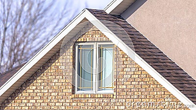 Panorama Close up of a home exterior with sunlit pitched roof over window and brick wall Stock Photo