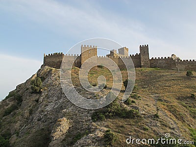Panorama of the fortress wall with battlements in the rays of the setting sun, and a rock with grass faded in the sun against a bl Stock Photo