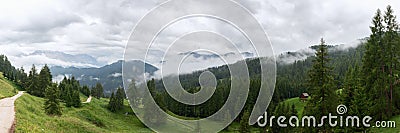 A panorama of the Italian Dolomites covered with fog and a hiking trail through the forest Stock Photo