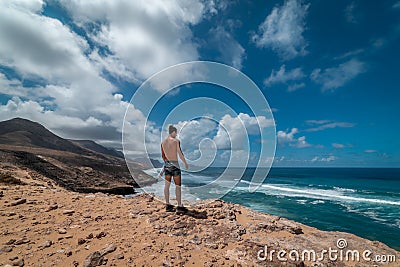Young traveler crosses the dunes of the jandia natural park in fuerteventura canary islands and contemplates in the background t Stock Photo