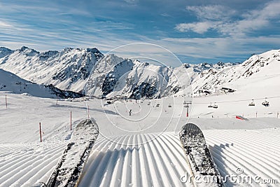 Panorama point of view skier legs on downhill start straight line rows freshly prepared groomed ski slope piste on bright day blue Stock Photo
