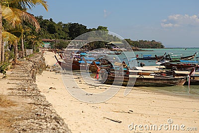 Panorama seascape dayshot of a white yellow sand beach with long boats, palm trees, mountains, turquoise ocean water and a blue Editorial Stock Photo