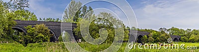 A panorama view of cows grazing on the banks of the River Nene in front of the old railway viaduct at Thrapston, UK Stock Photo