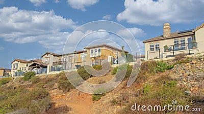 Panorama White puffy clouds Dirt uphill trail on a rocky slope outside the fenced homes at S Stock Photo