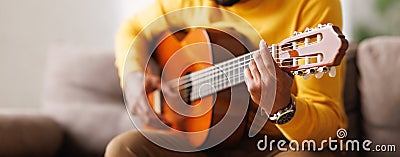 Panoramic banner with man playing on acoustic guitar, sitting on sofa at home Stock Photo