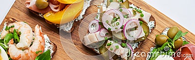 Panoramic shot of delicious smorrebrod sandwiches on wooden chopping board on white. Stock Photo