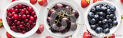 Panoramic shot of fresh and ripe cherries, blueberries and cranberries on bowls and strawberries on background. Stock Photo