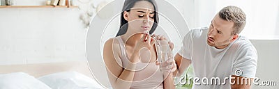 Shot of wife with pain taking pill with water in bedroom with husband near Stock Photo