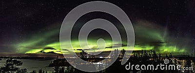 Panoramic view of of brilliant green Aurora. It is curved above horizon line, shining over Scandinavian landscape with frozen Stock Photo