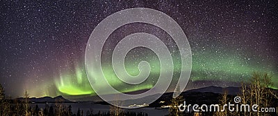 Panoramic view of multicolored Aurora curved above Scandinavian mountains and frozen lake, very cold winter night, deep clear sky Stock Photo