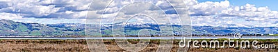 Panoramic view towards green hills and snowy mountains on a cold winter day taken from the shores of a marsh in south San Stock Photo