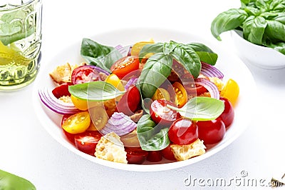 Panzanella summer vegetable salad with stale bread, colorful tomatoes, red onion, olive oil, salt and green basil, white table Stock Photo