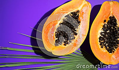 Papaya fruit on tropical violet background with palm tree leaf. Halved fresh organic Papayas Stock Photo