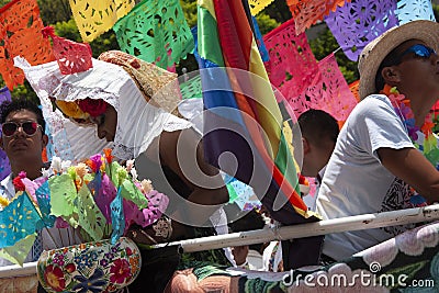 Among papel picado protesters of the LGBTTTI pride march ride on allegorical car adorned with rainbow colors wearing hats and sun Editorial Stock Photo