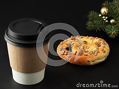 Paper cup with a hot drink, coffee or tea on a black background. Near a fresh pretzel and a Christmas tree. Close-up. Horizontal Stock Photo