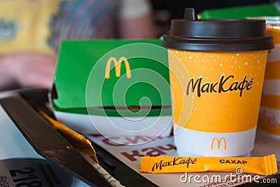 A paper cup of McDonald`s coffee with the inscription Maccafe in Russian and a hamburger in a box on a tray. Fast food restaurant Editorial Stock Photo