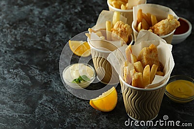 Paper cups with fried fish and chips, and sauces on black smokey background Stock Photo