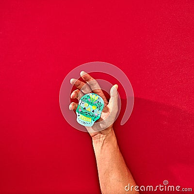 The hand of a man holds a handcraf paper skull Calaveras attributes of the Mexican holiday Calaca on a red background Stock Photo