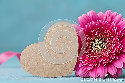 Paper heart tag and beautiful pink gerbera flower on turquoise table. Greeting card for Birthday, Woman or Mothers Day. Stock Photo