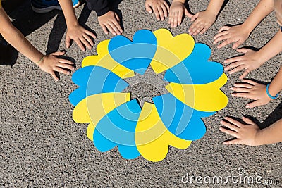 paper hearts in yellow and blue and many children's hands around on sunny day Stock Photo