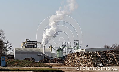 Paper mill with steaming chimney and large stacks of whole tree trunks in the square in front Stock Photo