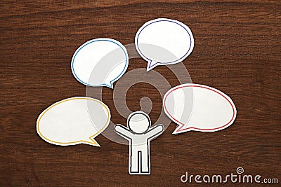 Paper person with colorful blank dialog speech bubbles on brown wood. Communication concept. Stock Photo