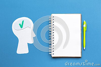 A paper silhouette of a thinking human head. Notebook with pen on a blue background. Mock up. Flat lay. Concept of Stock Photo