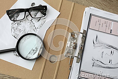 Papers with suspect`s portrait, palm print and magnifying glass on wooden table in detective office, top view Stock Photo