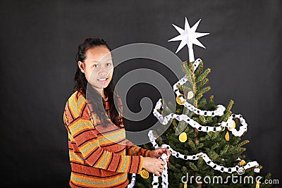 Papuan girl putting white paper chain on Christmas tree Stock Photo